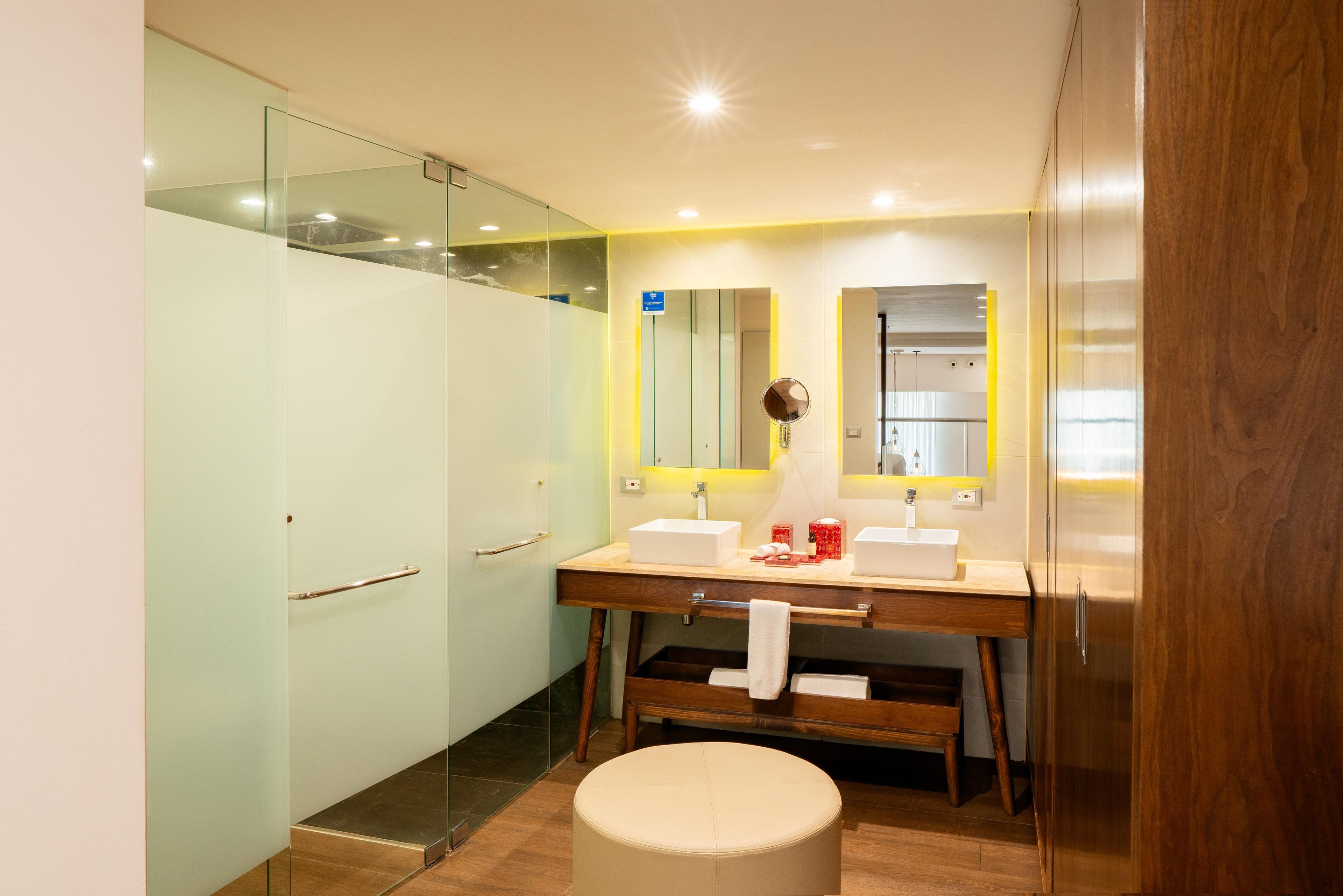 A modern bathroom with a glass shower enclosure, dual sinks, and a wooden vanity.