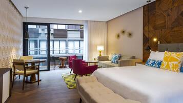 Quarto de hotel com uma cama grande, um sofá, uma mesa de jantar com cadeiras, uma varanda com vista para edifícios e uma parede com padrão.