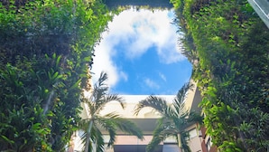 A modern building with a central atrium surrounded by lush greenery and palm trees.