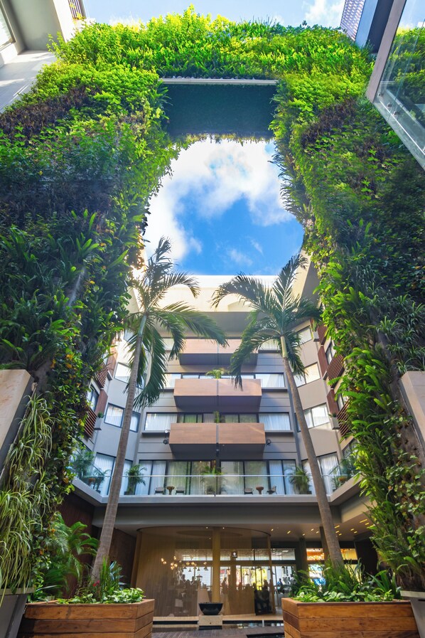 A modern building with a central atrium surrounded by lush greenery and palm trees.