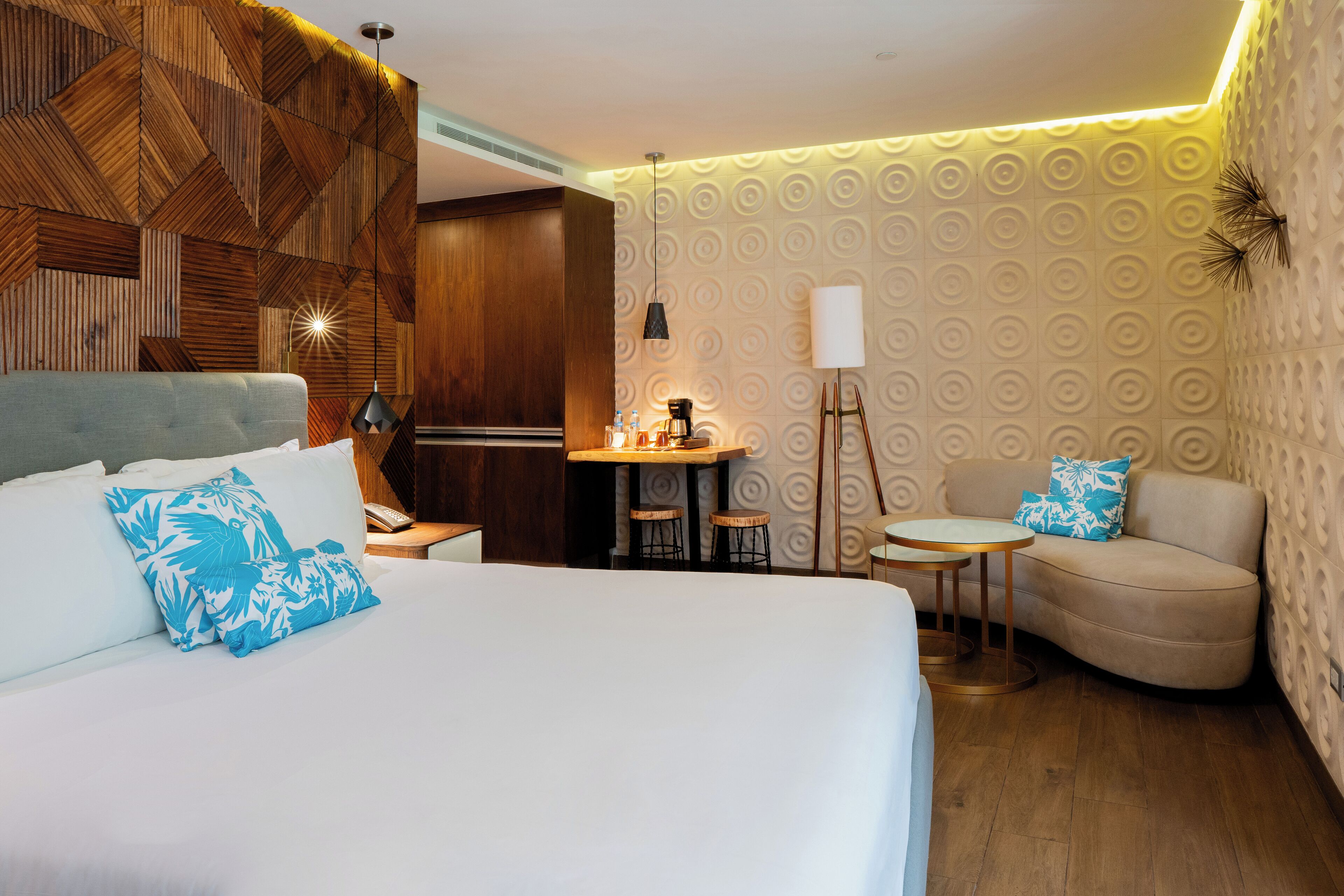 Une chambre d’hôtel avec un grand lit, un canapé, une petite table avec une lampe et un mur décoratif en bois.