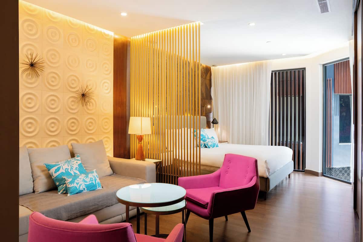 Ein modernes Hotelzimmer mit einer Couch, zwei rosa Stühlen, einem Bett und einer Wand mit kreisförmigen Mustern.