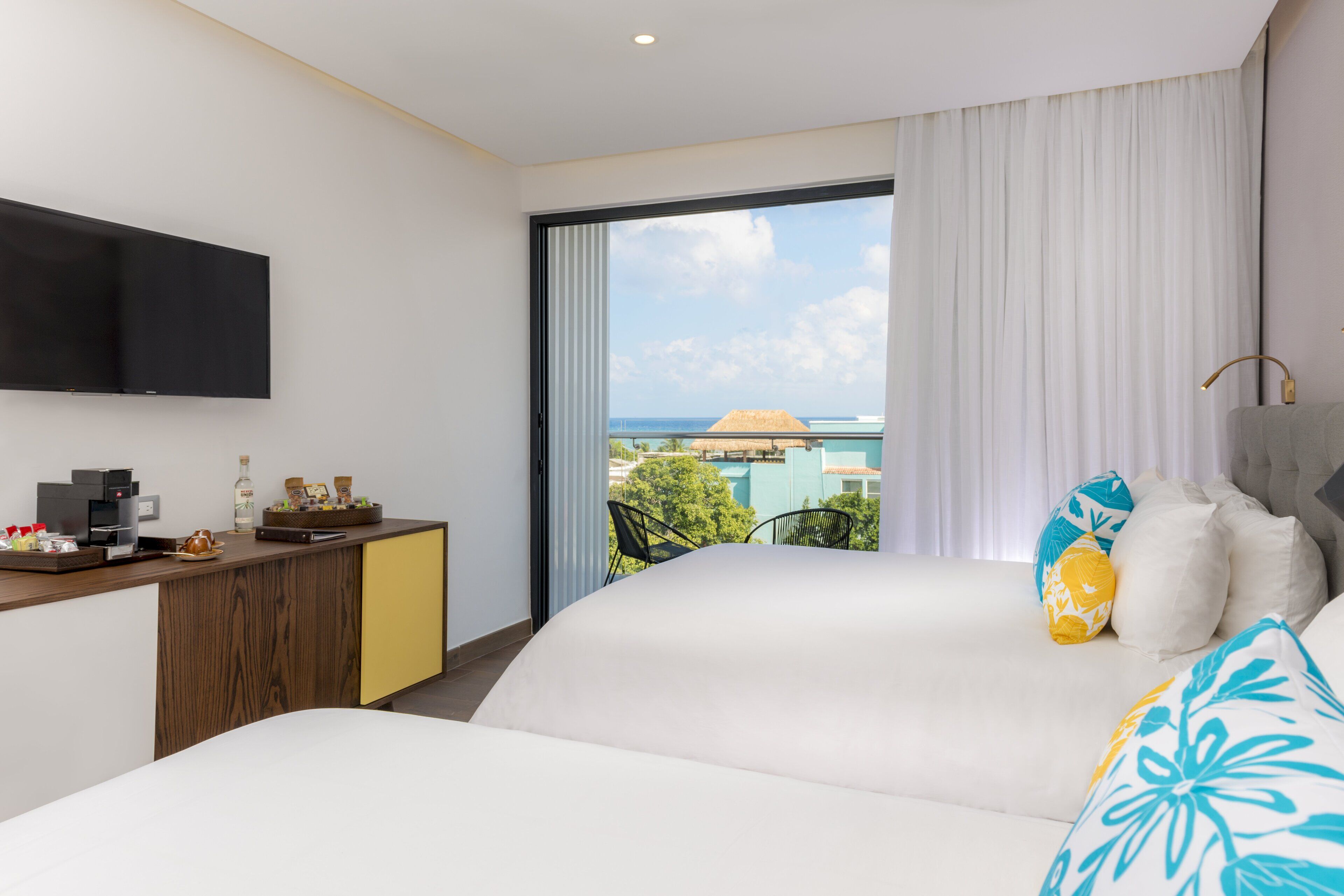 Een hotelkamer met een bed, een bureau met een flatscreen-tv, een koffiezetapparaat en uitzicht op de oceaan.
