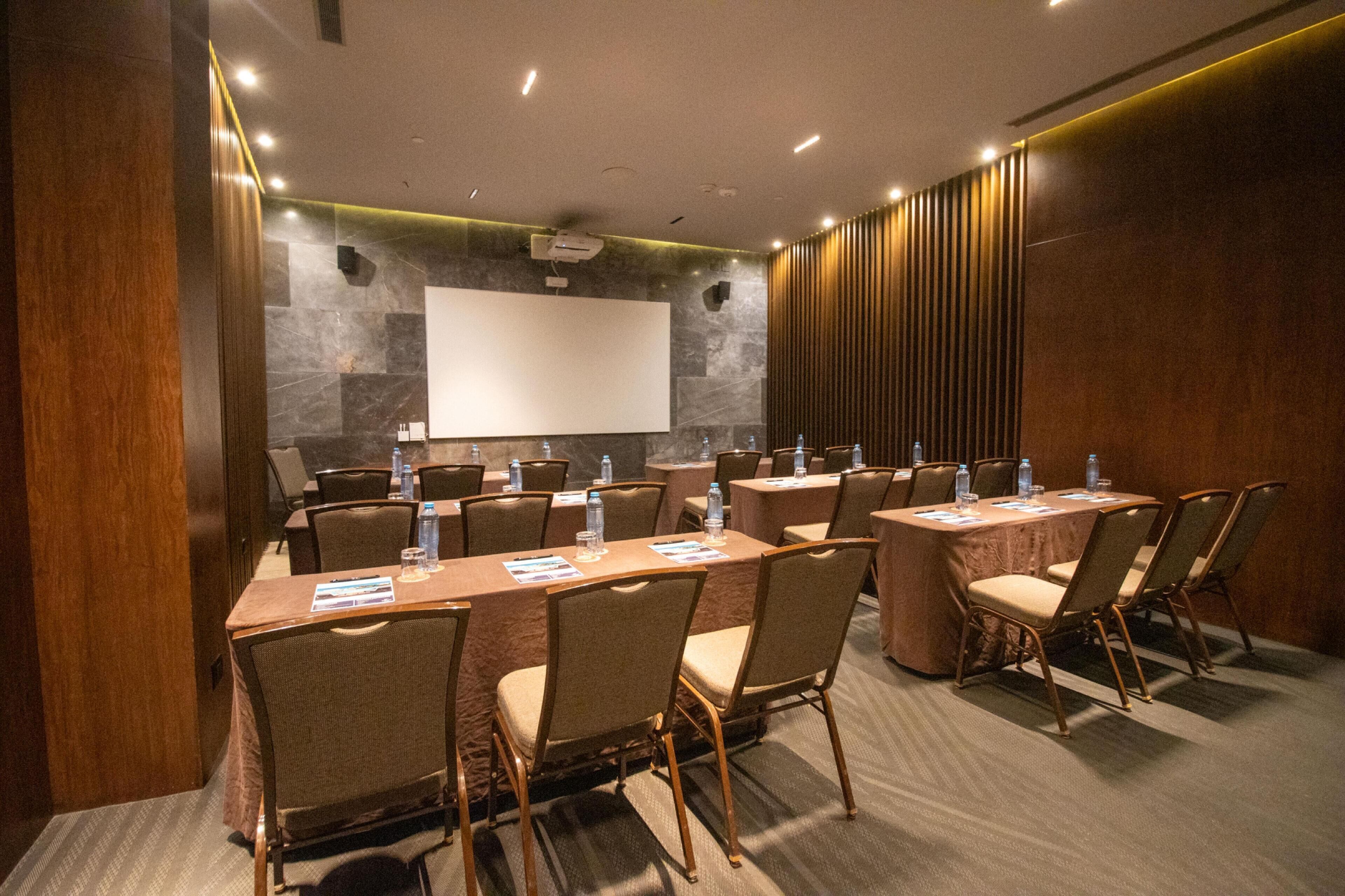 A conference room with multiple tables and chairs, equipped with water bottles and a projector screen.