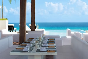 A table set for dining with a view of the ocean, white furniture, and a clear sky. - The Fives Downtown Hotel - Curio Collection by Hilton (Playa del Carmen)