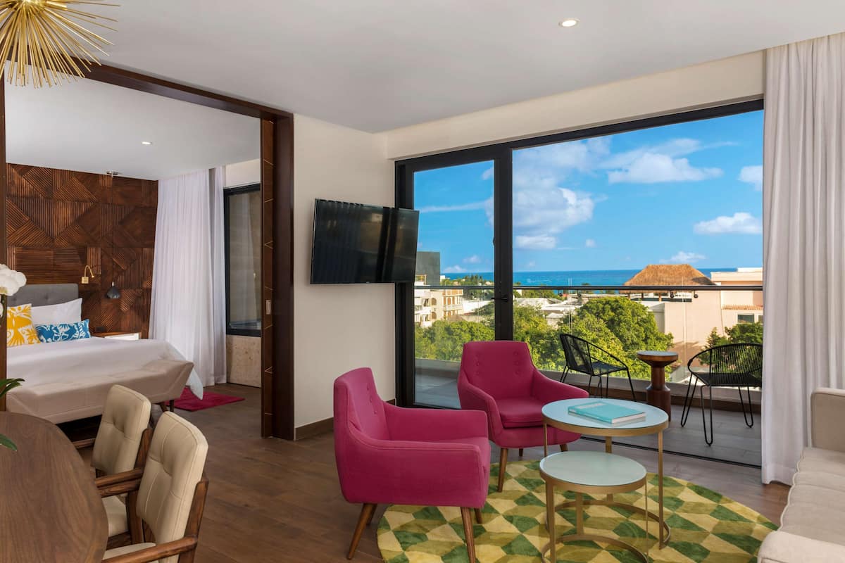 Ein modernes Hotelzimmer mit einem großen Balkon, einem Bett, einem Fernseher und einer Essecke mit Stühlen und einem Tisch.