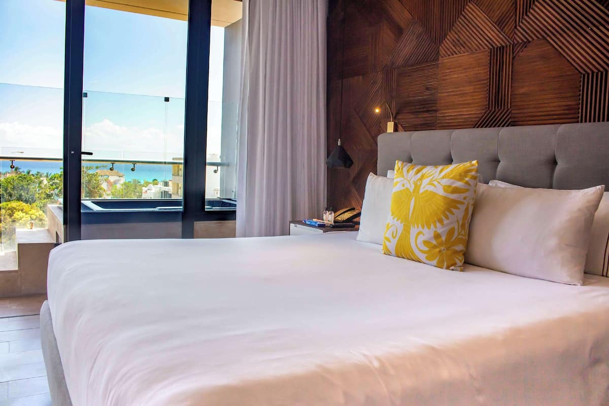 Ein Hotelzimmer mit einem großen Bett, Meerblick und einer Wandgestaltung aus Holz.