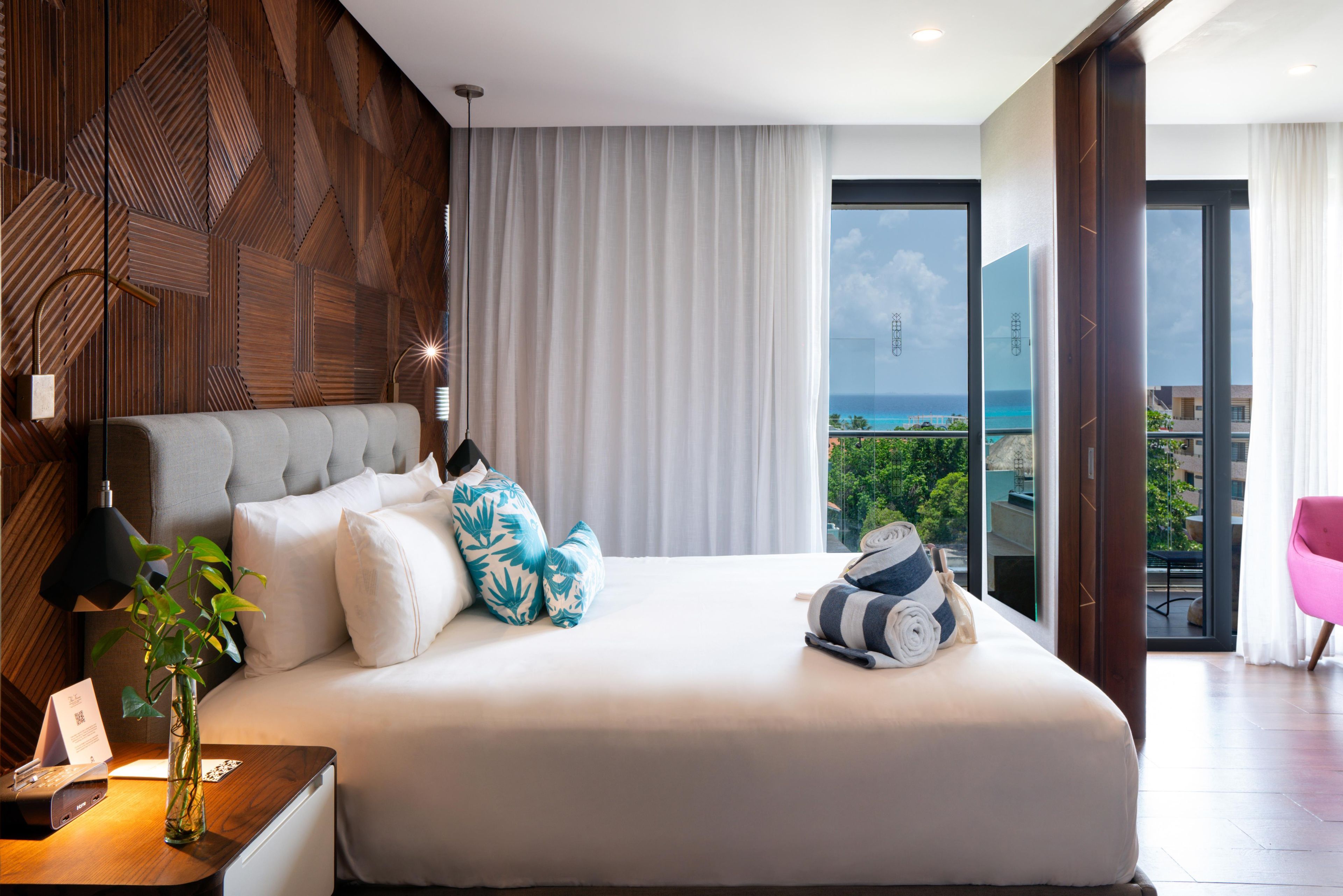 Une chambre d’hôtel moderne avec un grand lit, une vue sur l’océan et un balcon agrémenté d’une chaise rose.