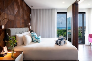 A modern hotel room with a large bed, a view of the ocean, and a balcony with a pink chair. - The Fives Downtown Hotel - Curio Collection by Hilton (Playa del Carmen)