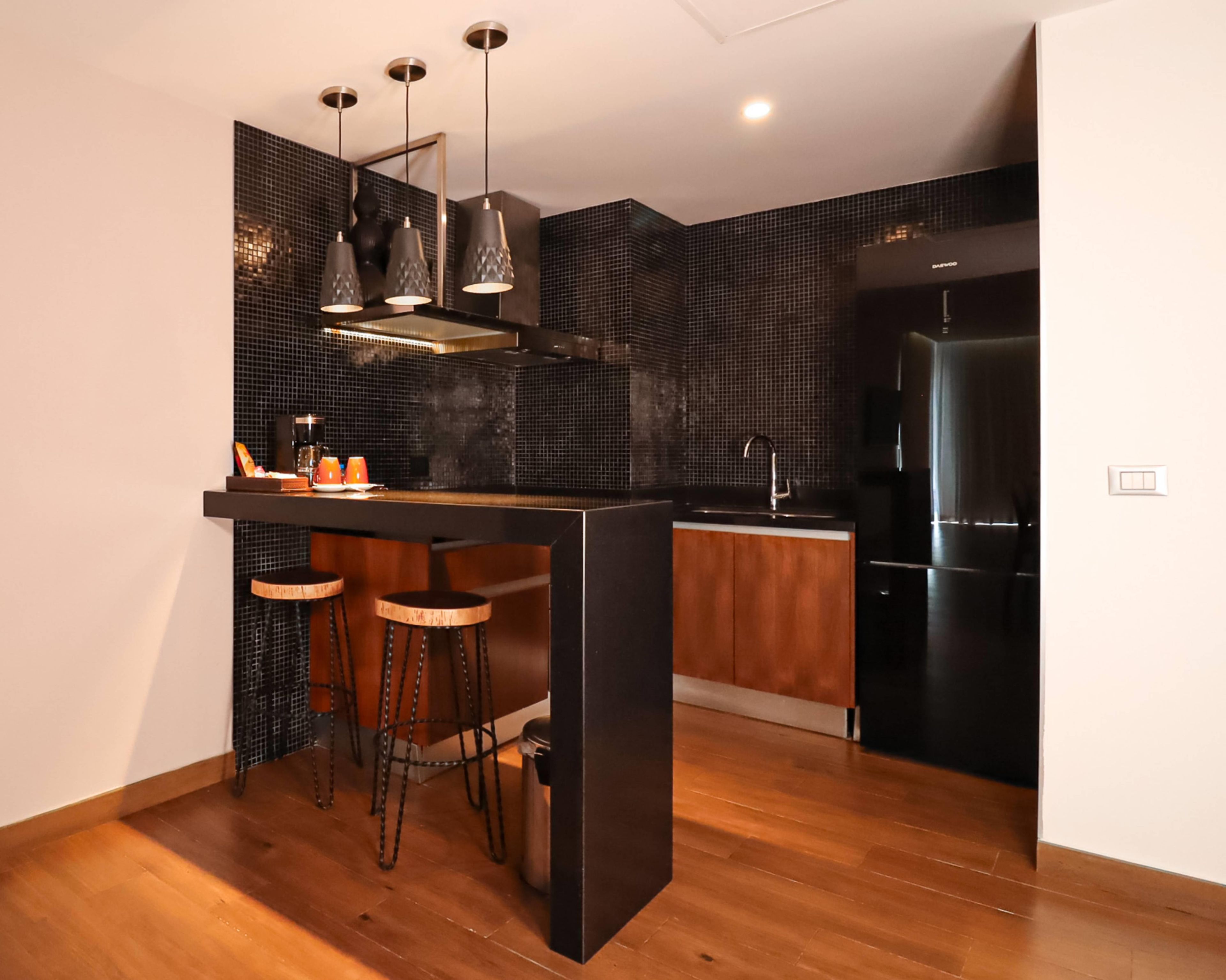 Une cuisine moderne avec un plan de travail noir, des tabourets en bois, un réfrigérateur en acier inoxydable et un pare-feu en carrelage.