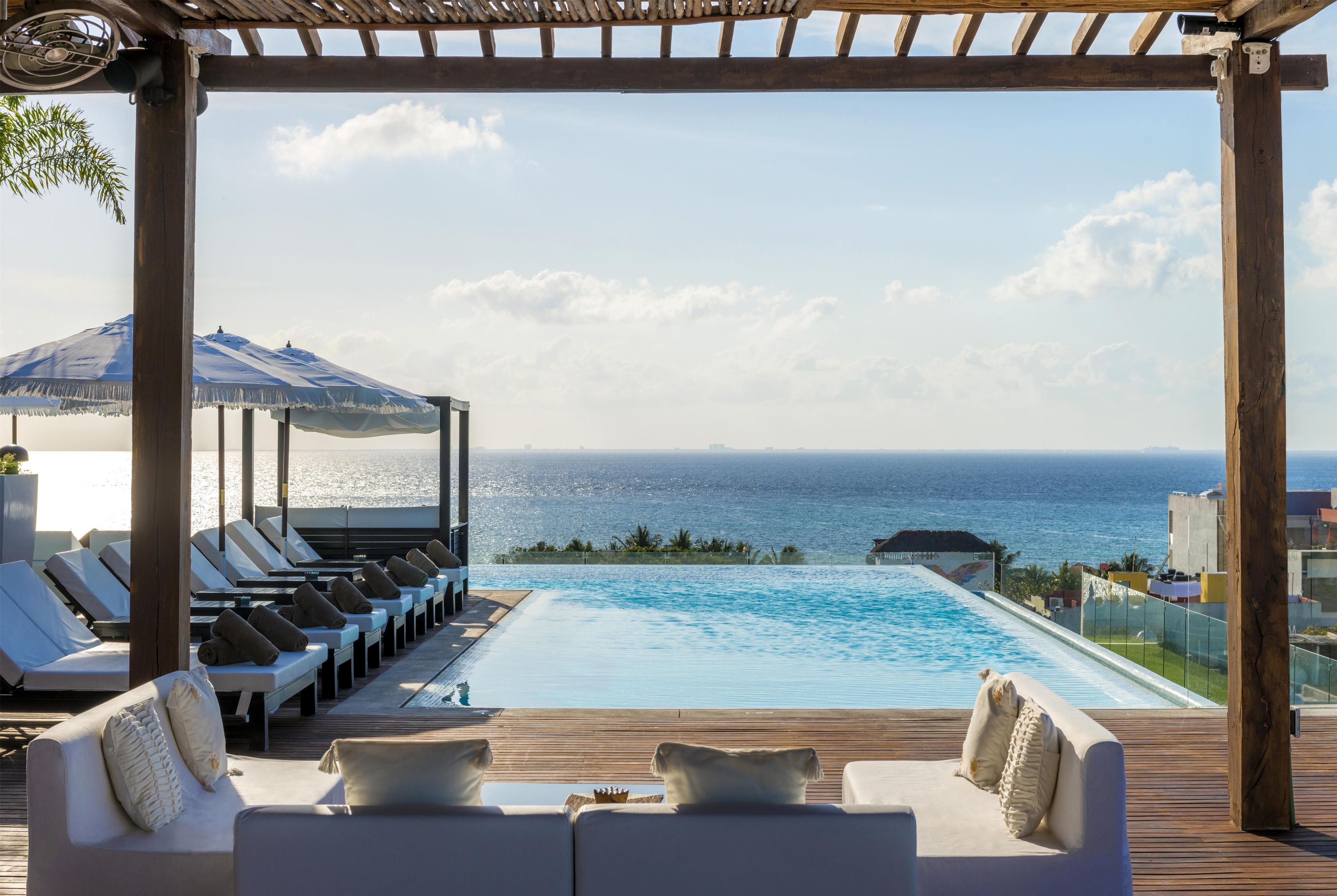 A poolside area with lounge chairs and a pergola overlooking the sea.