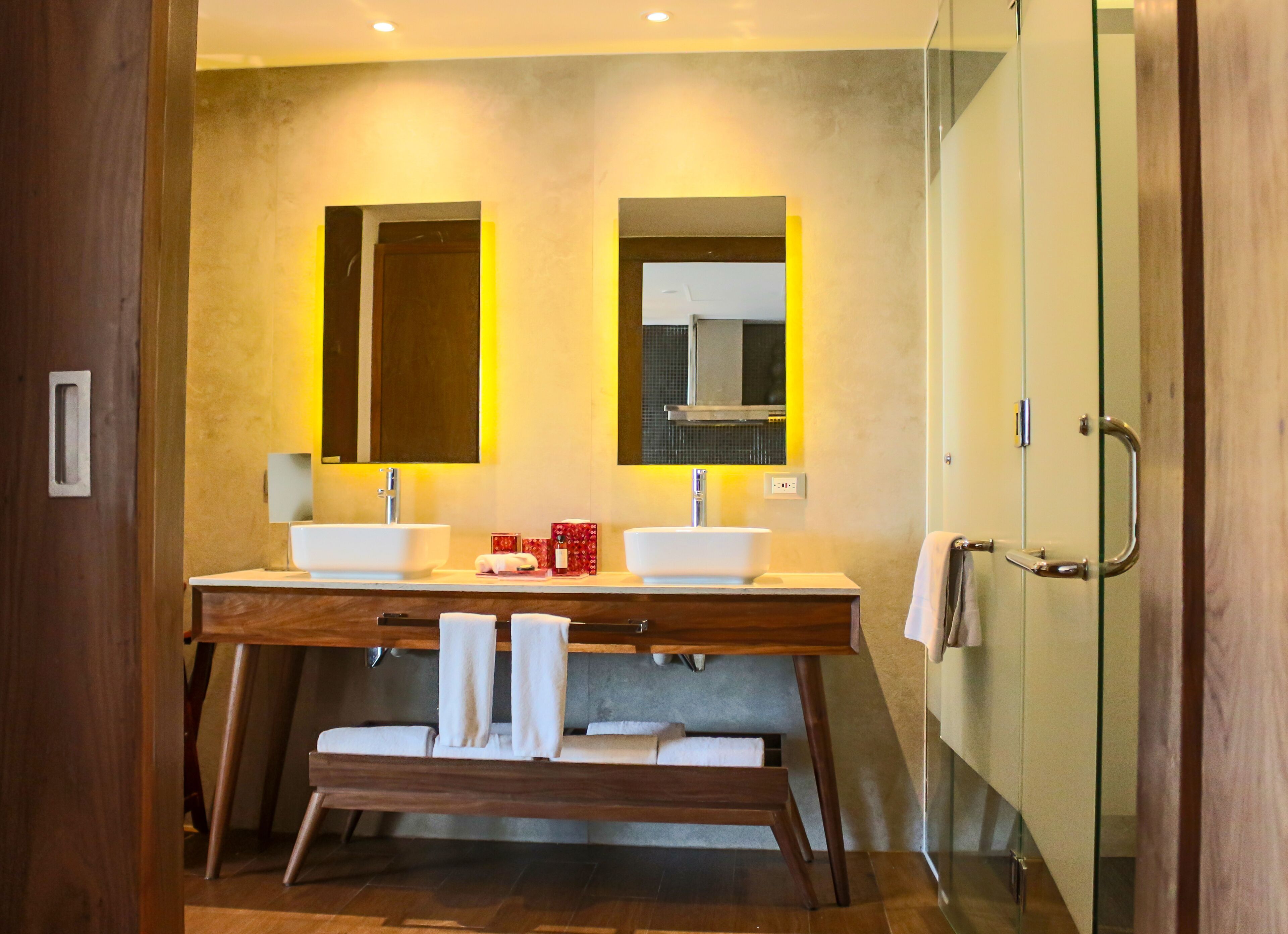 A modern bathroom with two sinks, a bench, and a glass shower enclosure.