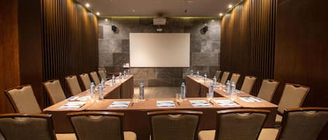 A conference room with a long table, chairs, a projector screen, and a stone wall.