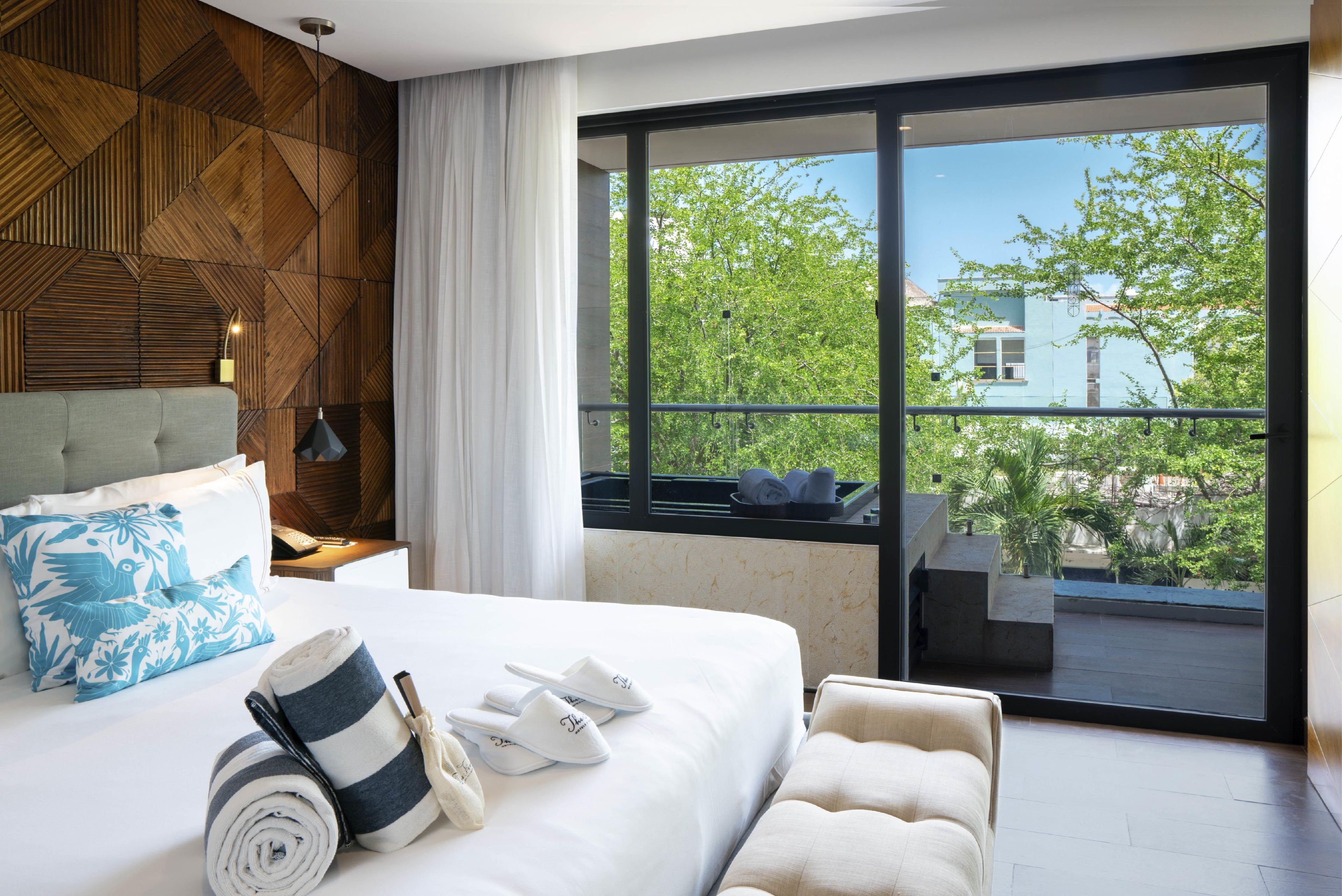 Habitación de hotel moderna con una cama grande, vista al exterior y un revestimiento de madera geométrico.