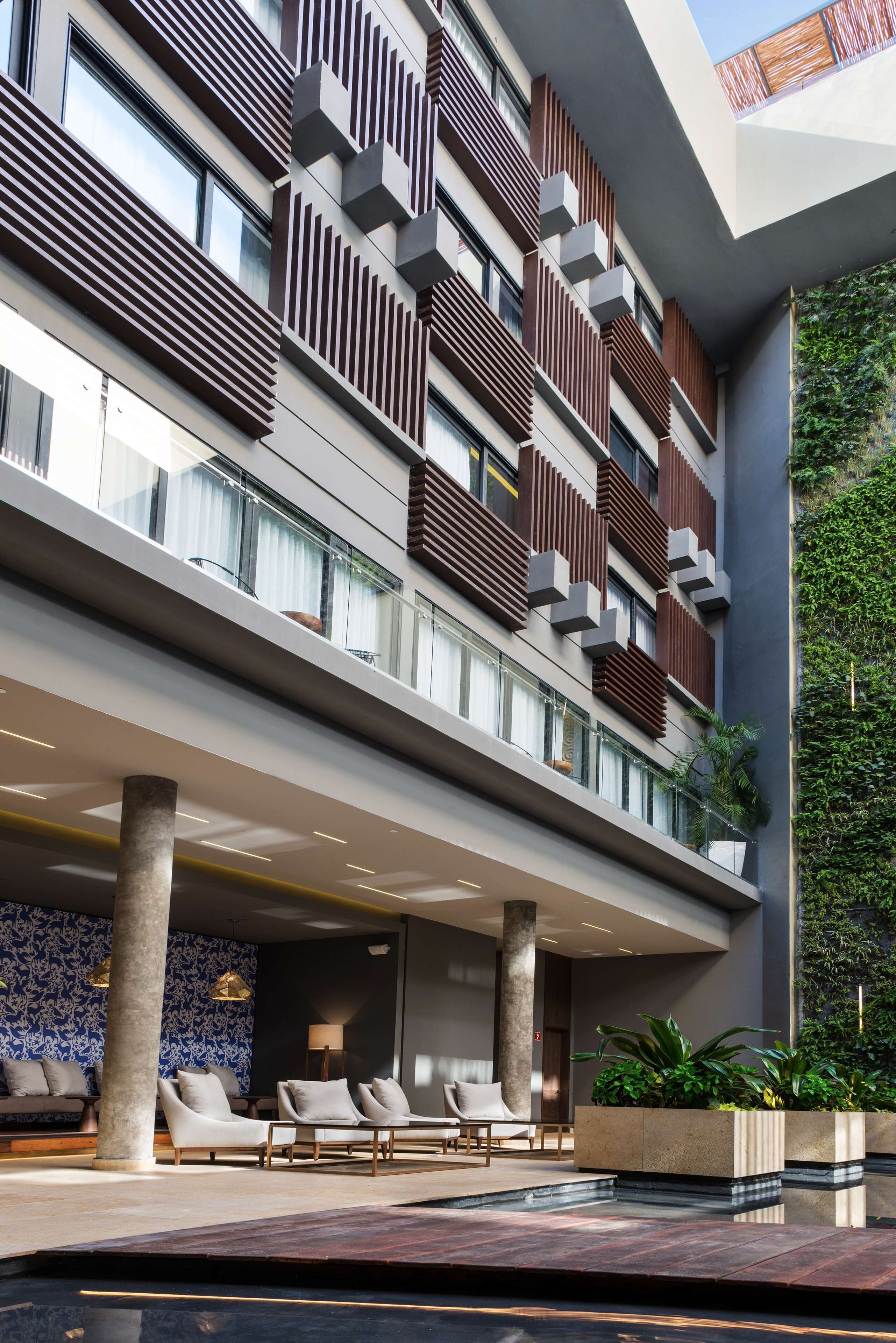 A modern hotel lobby with a spacious seating area, a pool, and a vertical garden.