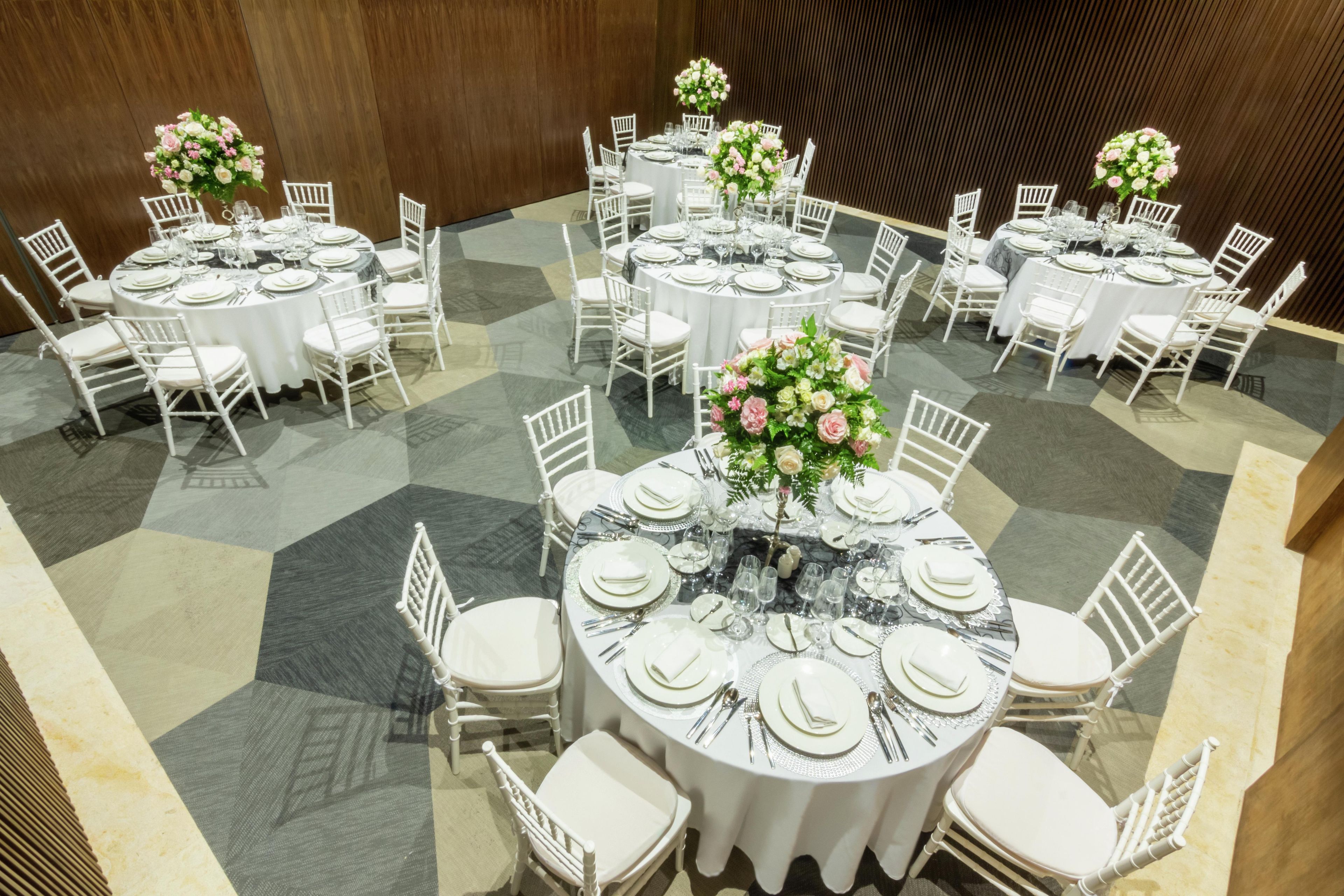 A banquet hall with round tables set for dining, white chairs, and floral centerpieces.