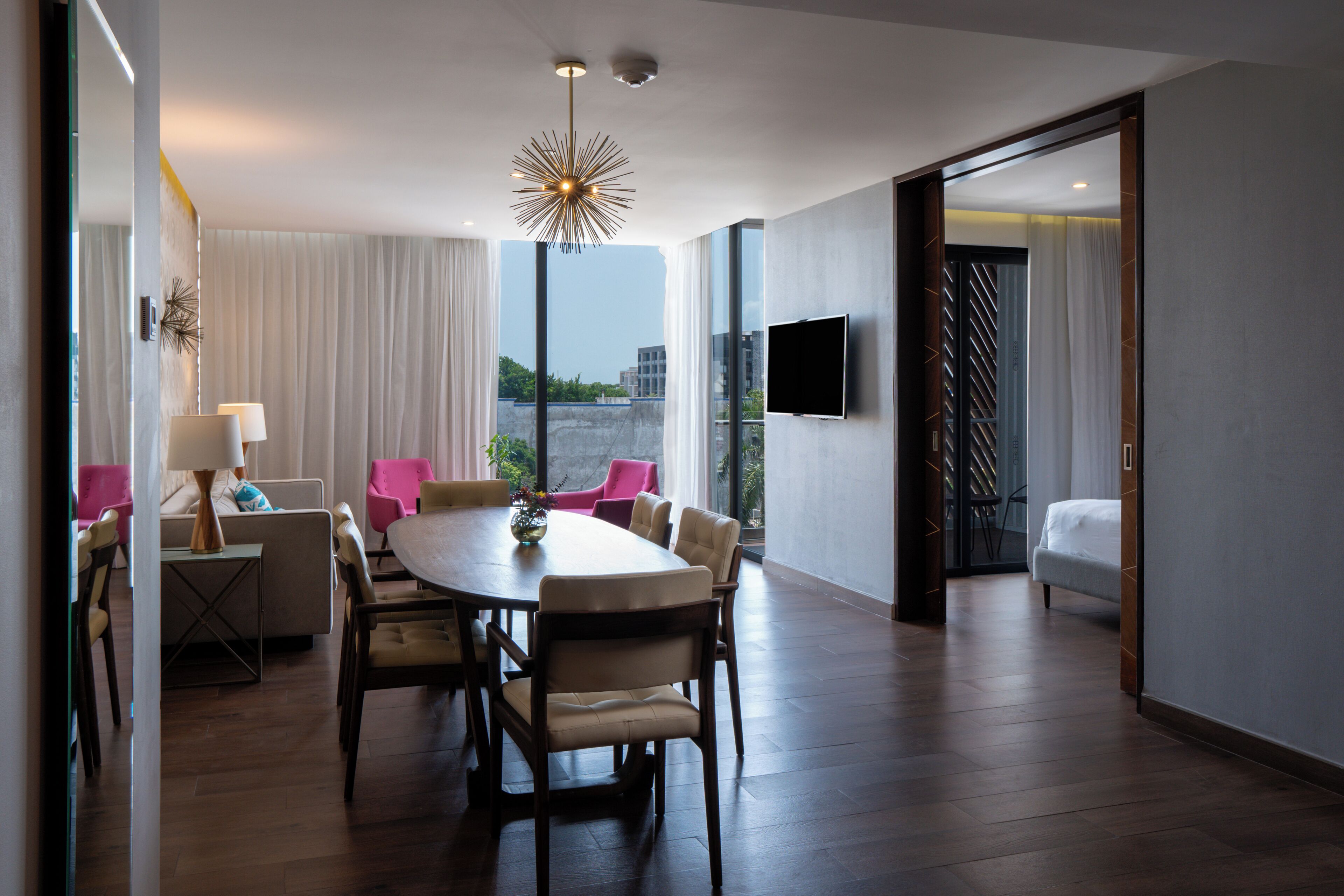 Habitación de hotel moderna con zona de comedor, un ventanal con cortinas, televisión de pantalla plana y una cama.
