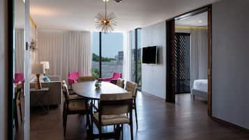 Habitación de hotel moderna con zona de comedor, un ventanal con cortinas, televisión de pantalla plana y una cama.