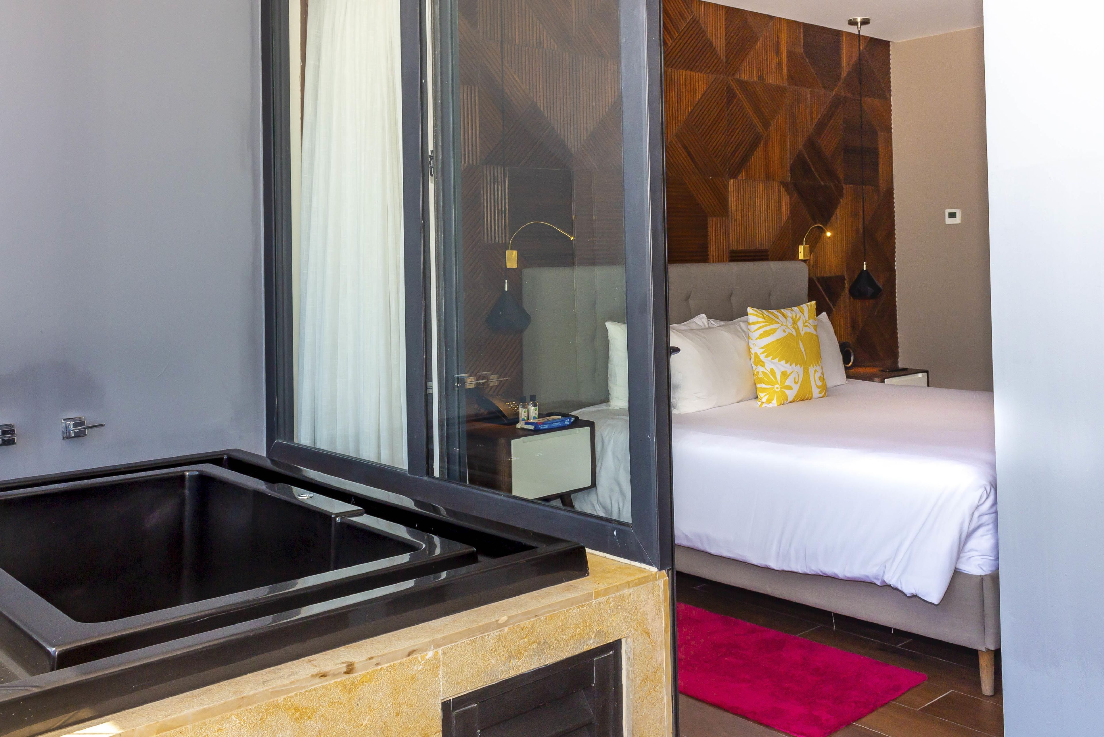 Une chambre d’hôtel moderne dotée d’un grand lit, d’une baignoire entourée de parois en verre et d’un mur décoratif en bois.