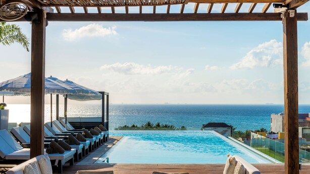 An infinity pool with lounge chairs and umbrellas, overlooking the sea.