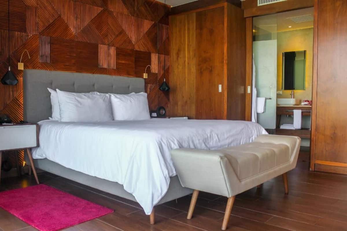 Ein modernes Schlafzimmer mit einem großen Bett, einem Nachttisch, einer Bank und Holzvertäfelung an der Wand.