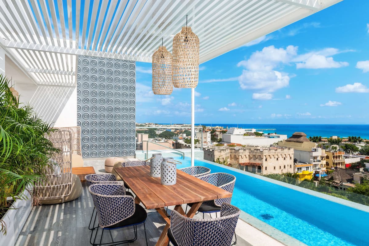 Eine Dachterrasse mit Holztisch und -stühlen, einem Pool und Blick auf Stadt und Meer.