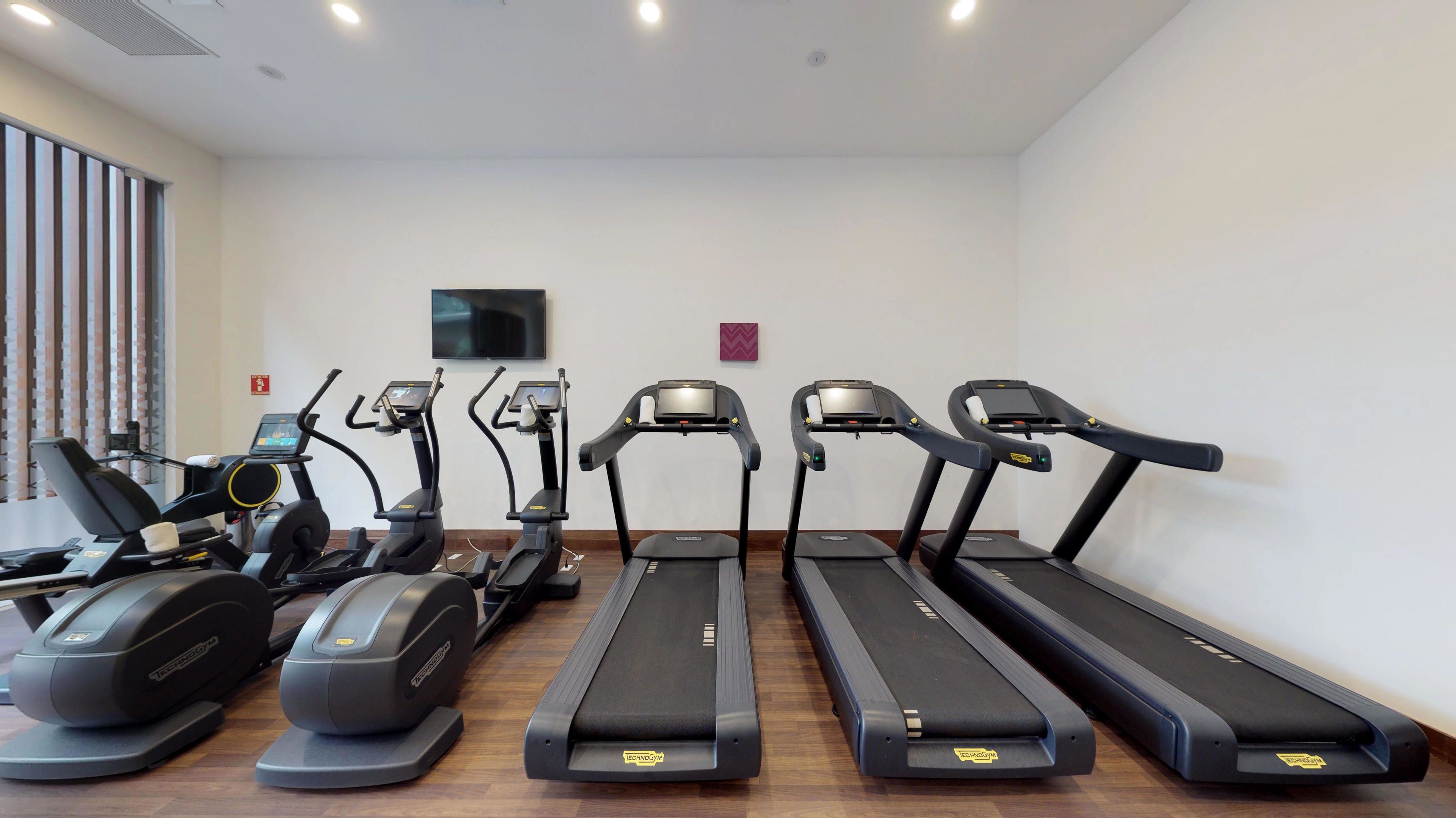 Un gimnasio con cintas de correr, una bicicleta estática y una máquina de remo.