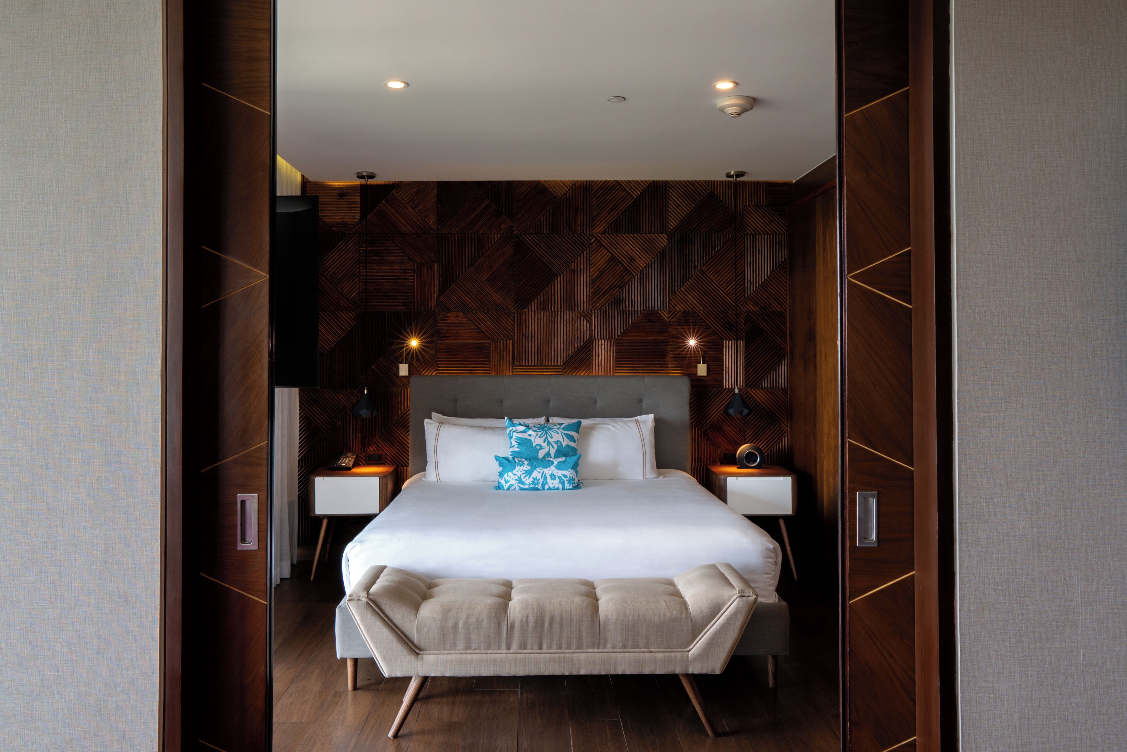 A modern bedroom with a large bed, wooden paneling on the walls, and two bedside tables with lamps.
