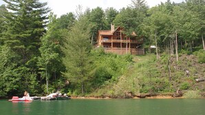 Eine große Holzhütte mit Balkon, umgeben von dichtem Wald und einem See.