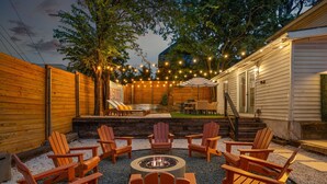 Eine Terrasse im Freien mit Adirondack-Stühlen, einem Feuerkorb und Lichterketten.