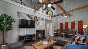 A spacious living room with a fireplace, a television, and a dining area with red curtains. - Huge Bachelor/ettes & family property w/ 2 Homes, Pool, Games, close to Downtown (Austin)