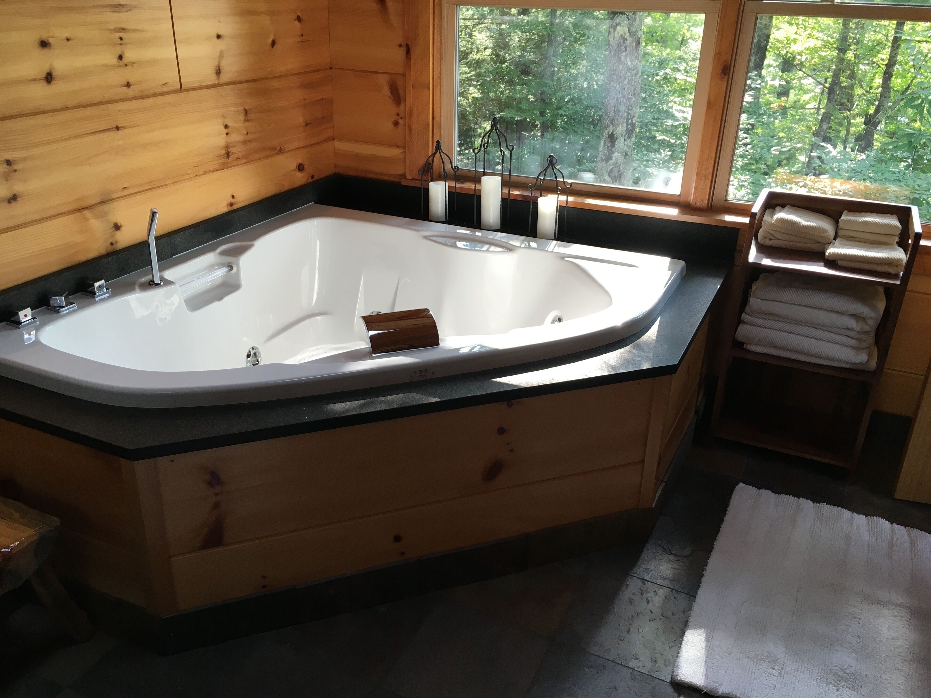 A wooden cabin bathroom with a freestanding bathtub, a window with a view of trees, and a towel rack with folded towels.