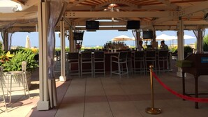 Un área de bar al aire libre con vista al mar, que incluye una barra, sillas y sombrillas.
