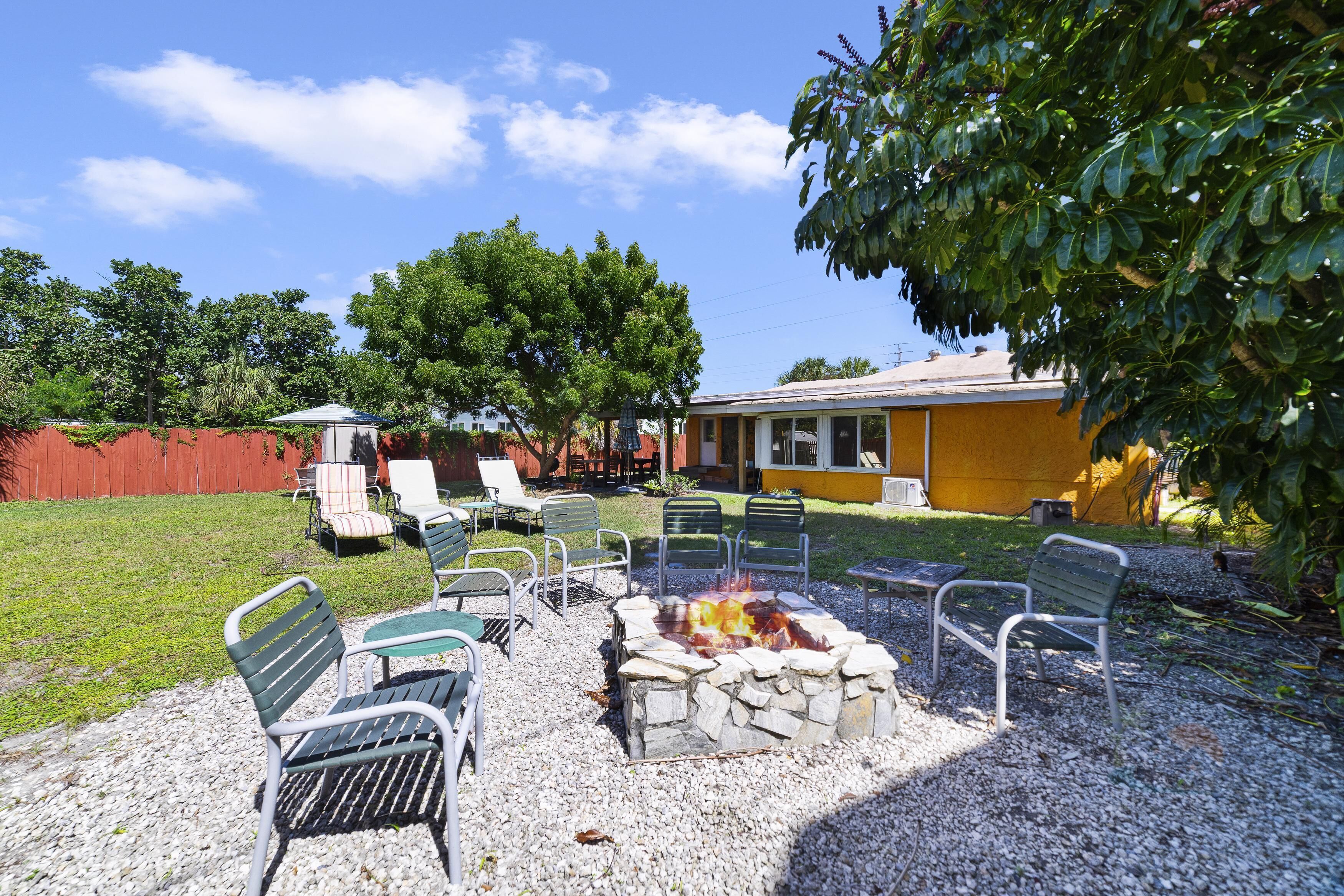 Un patio con mobiliario exterior, una fogata y un edificio amarillo al fondo.