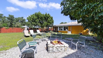 Un patio con mobiliario exterior, una fogata y un edificio amarillo al fondo.