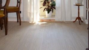 Une pièce comprenant une chaise en bois, une petite table, une plante en pot et un tableau encadré accroché au mur.