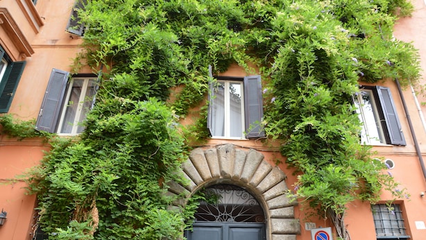 Une façade d’immeuble avec une entrée centrale en arc de cercle, de nombreuses fenêtres avec volets et un panneau indiquant qu’il est interdit de se garer.