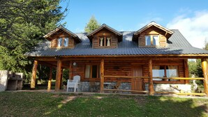 A wooden cabin with a porch, stone wall, and a metal roof. - Cabañas La Pampita (Villa La Angostura)