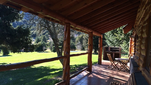 A covered outdoor area with a wooden deck, a grill, and a bench. - Cabañas La Pampita (Villa La Angostura)