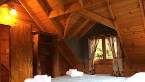 A wooden cabin room with a bed, a window with curtains, and a door. - Cabañas La Pampita (Villa La Angostura)
