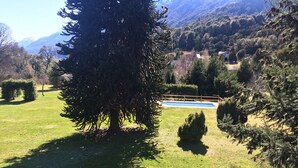 A large evergreen tree in a well-maintained grassy area with a pool and a wooden fence. - Cabañas La Pampita (Villa La Angostura)