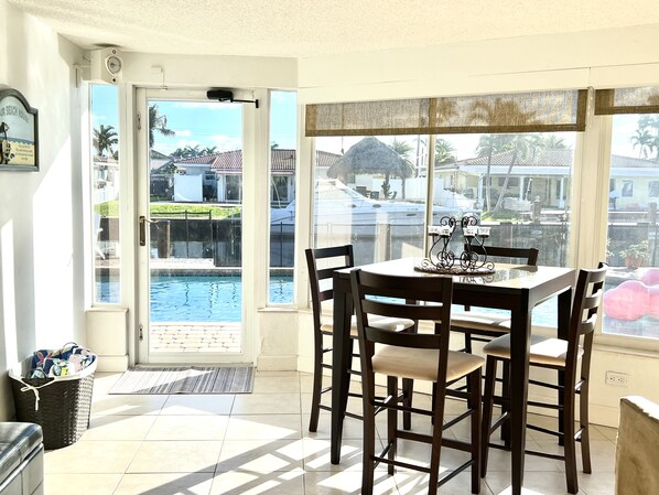 A dining area with a table and chairs, a view of a swimming pool, and a door leading outside. - Waterfront Home, Large Heated Pool, 5 min. from the beach, family friendly (Pompano Beach)