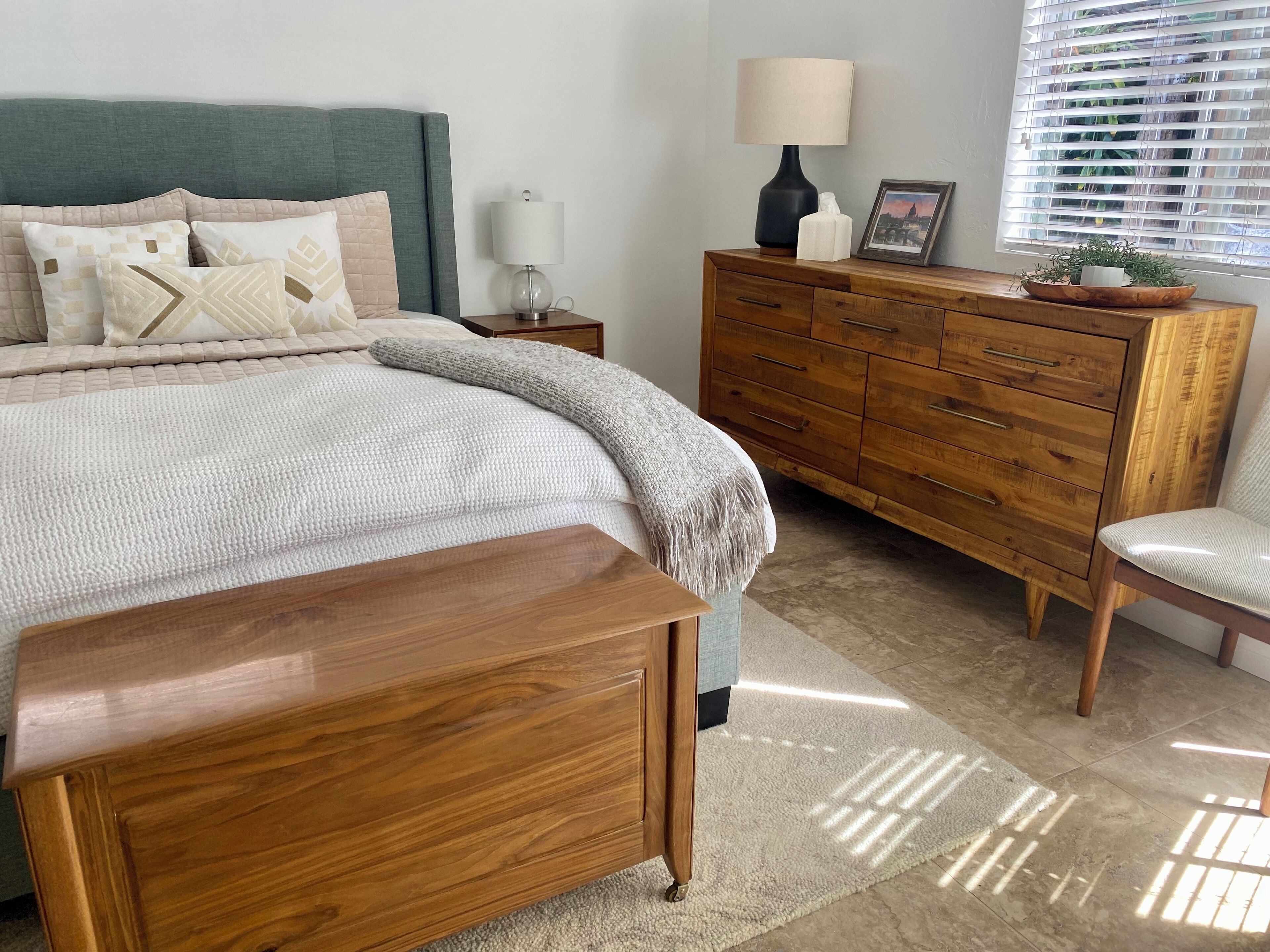 Un dormitorio con cama, mesita de noche, cómoda, silla y ventana con persianas.