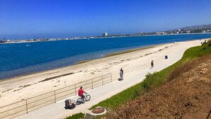 A coastal walkway with a clear view of the sea, a sandy beach, and a distant cityscape. - Crown Point Beach Oasis - 2 Blocks to the Bay!! (San Diego)