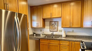 A kitchen with wooden cabinets, a stainless steel refrigerator, a granite countertop, a dishwasher, and a painting on the wall. - Crown Point Beach Oasis - 2 Blocks to the Bay!! (San Diego)