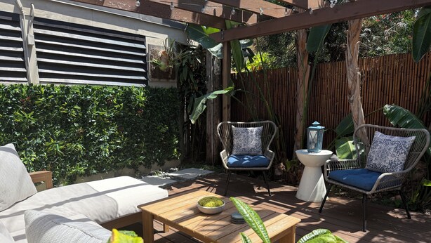 A patio with a wooden table, two wicker chairs with cushions, a white sofa, and lush greenery. - Crown Point Beach Oasis - 2 Blocks to the Bay!! (San Diego)