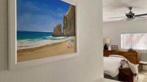 A framed painting of a beach scene with two people under an umbrella, a ceiling fan, and a bed with a white blanket in a room. - Crown Point Beach Oasis - 2 Blocks to the Bay!! (San Diego)