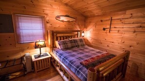 Ein gemütliches Holzblockhaus-Zimmer mit einem Bett, einem Nachttisch, einer Lampe und einem an der Wand aufgehängten Fisch.