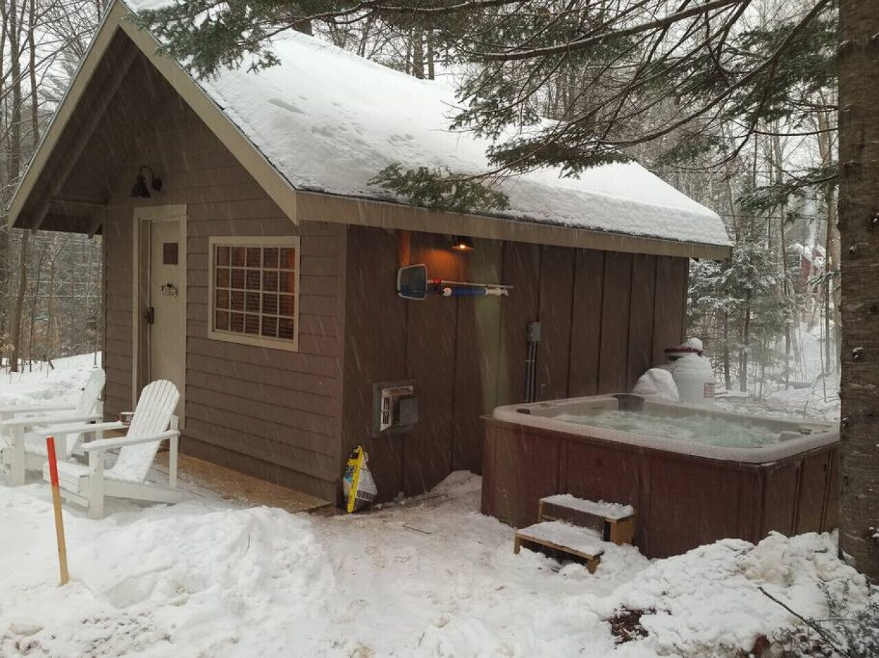 A wooden cabin with a hot tub and two Adirondack chairs outside.