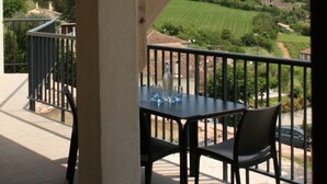 Un espacio al aire libre cubierto con una mesa y sillas, con vistas a un paisaje pintoresco con colinas y edificios.